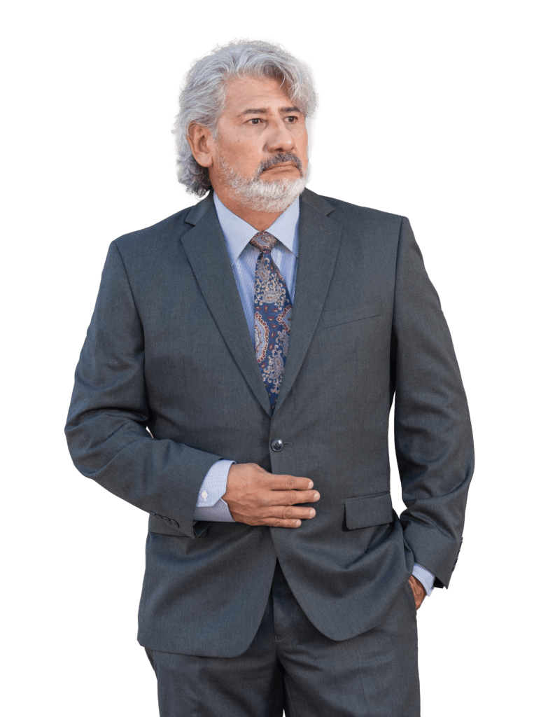 Man in a dark gray suit and patterned tie stands thoughtfully with hands on his waist. The image conveys professionalism and confidence.